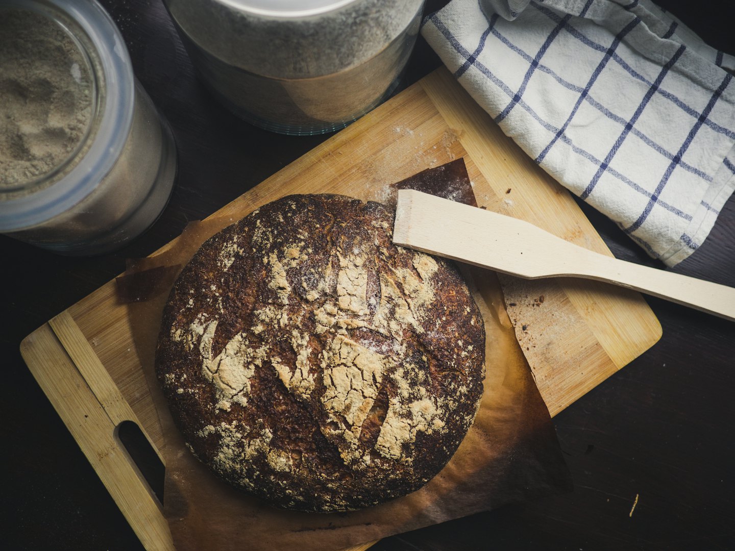 Dark artisan bread on a wooden cutting board with flour.