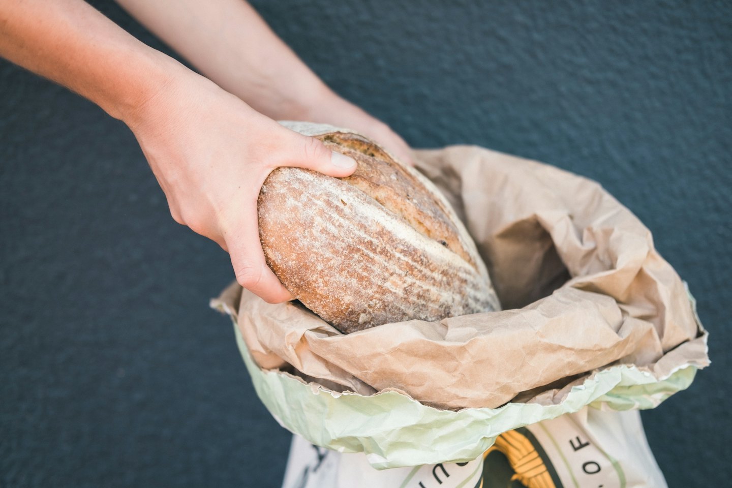 Hands holding a rustic sourdough loaf in a paper bag.