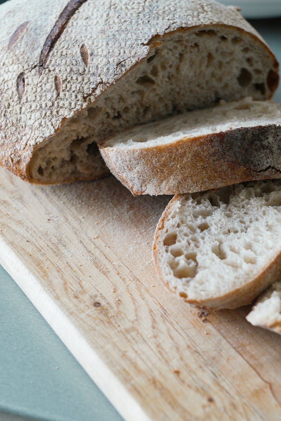 A sliced sourdough loaf rests on a floury wooden board.