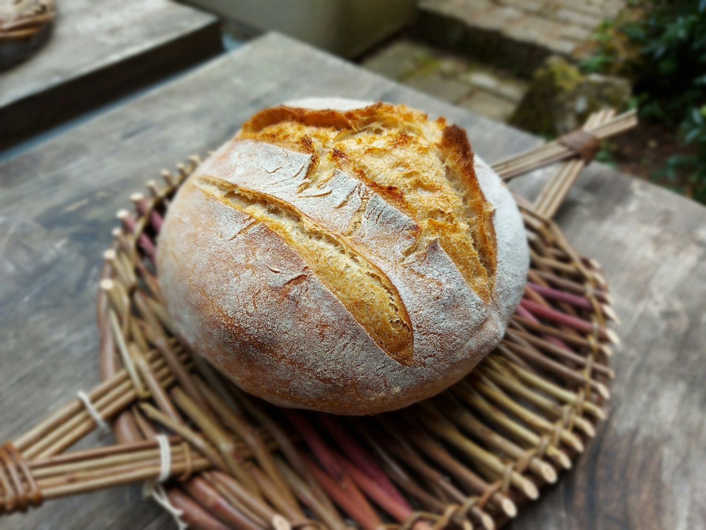 Freshly baked sourdough bread sits on a woven wicker tray.