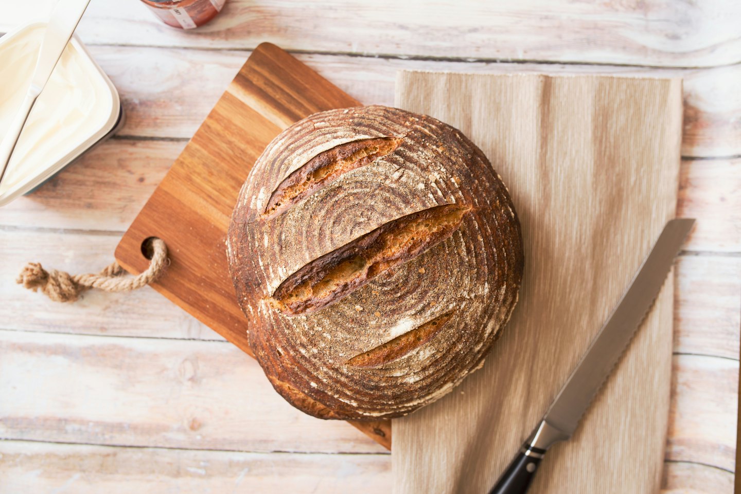 Artisan sourdough loaf on wooden board with knife and jam.